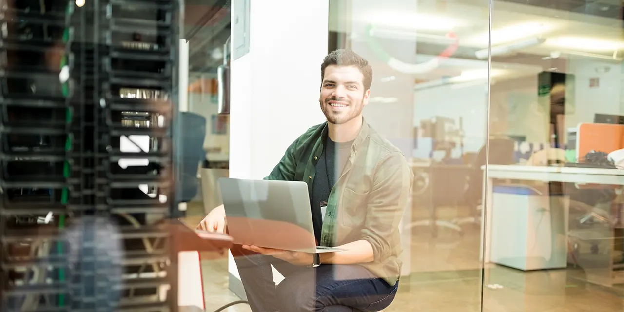 Técnico com notebook ao lado de um rack de servidores